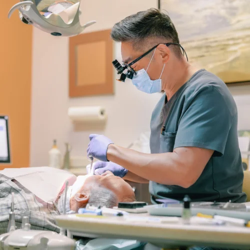 dentist wearing surgical mask and loupes performing a dental procedure on a patient