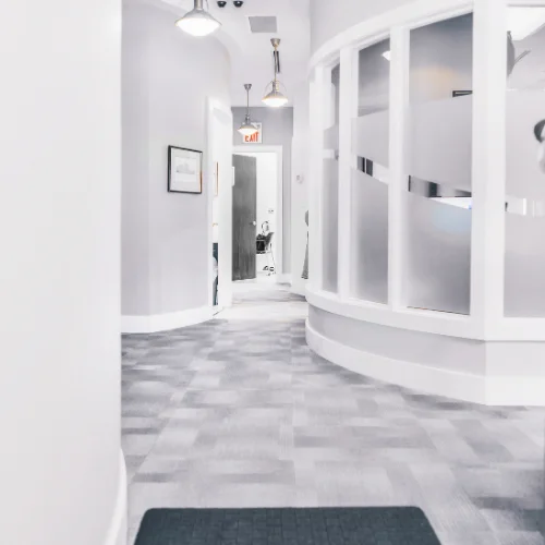 view down bright hallway of dental office featuring curved glass partition walls and modern lighting